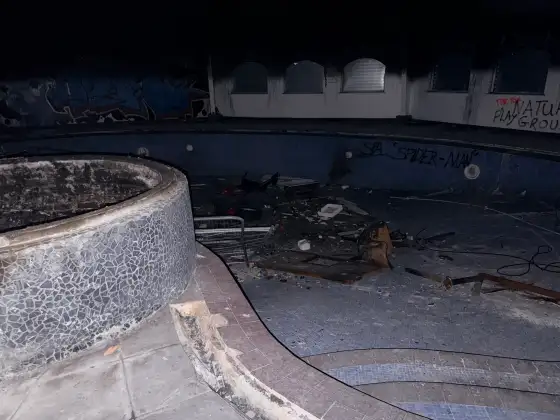 Circular tiled spa bath beside the empty swimming pool, with graffiti and scattered debris.