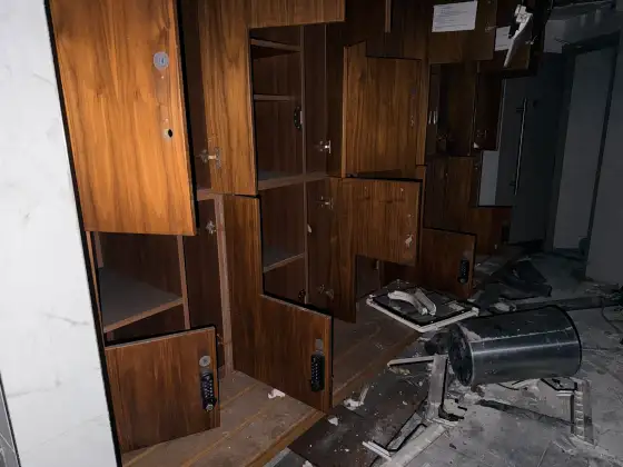 Open numbered wooden spa lockers with broken fixtures and ceiling material scattered across the floor.